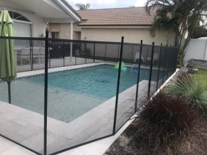 Black mesh pool fence along a pale deck beside a planting bed