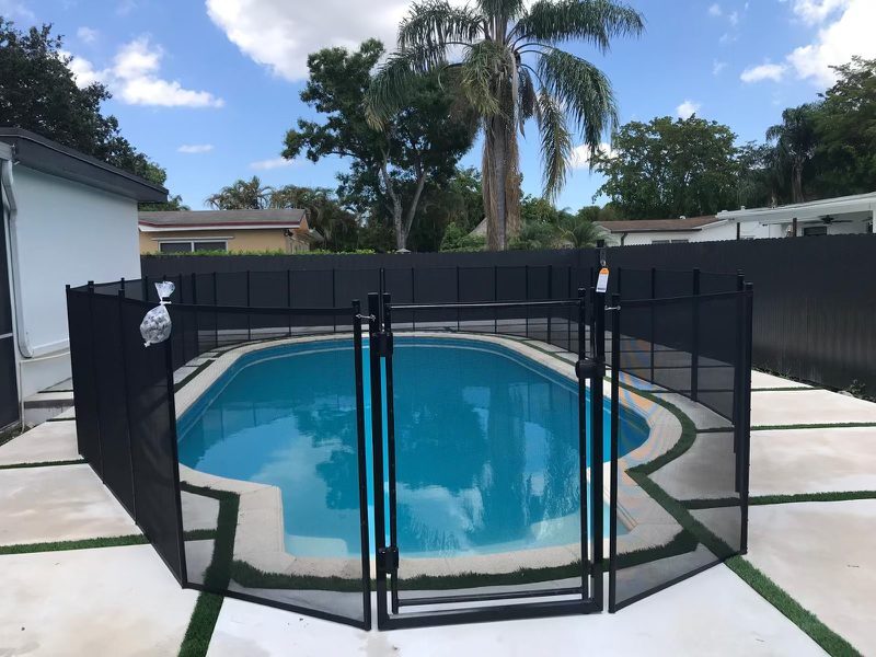 Black mesh gate centered at the end of a blue swimming pool