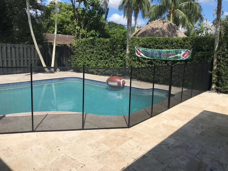 Black mesh pool fence following a curved blue pool beside a tropical backyard