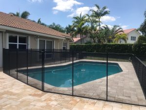 Black mesh pool fence around a blue backyard pool beside a tiled-roof house
