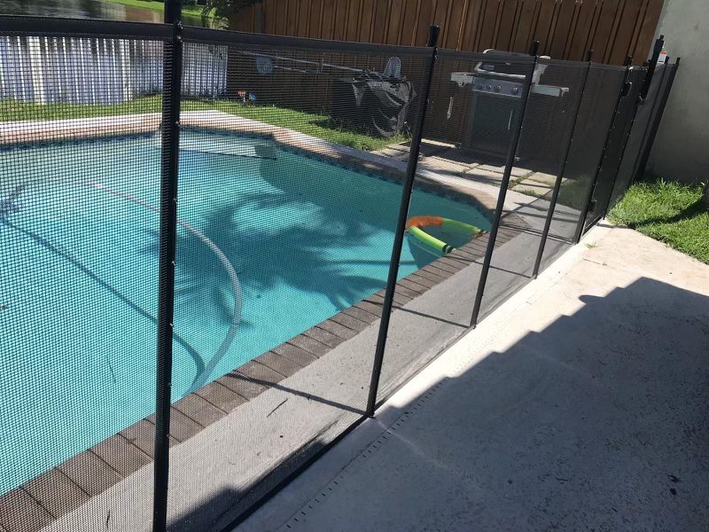 Black mesh pool fence and posts beside a blue pool and paved walking route