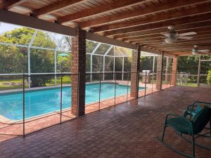 Beige removable mesh pool safety fence installed around a Miami backyard swimming pool.
