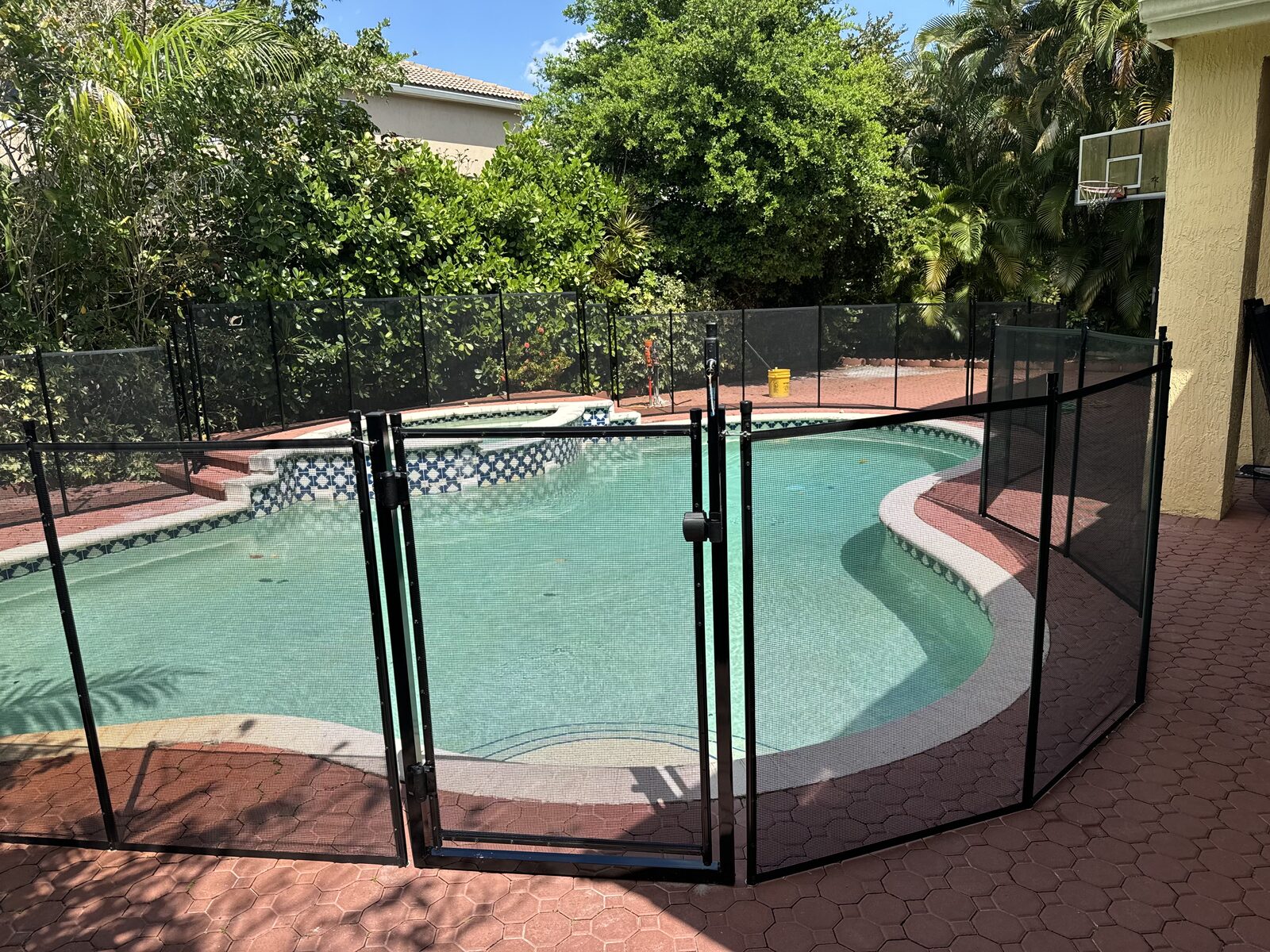 Pool fence storage planning reference: black mesh gate and adjoining fence beside a curved Pembroke Pines pool and spa