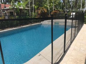 Black mesh pool fence posts along a rectangular pool and pale stone deck