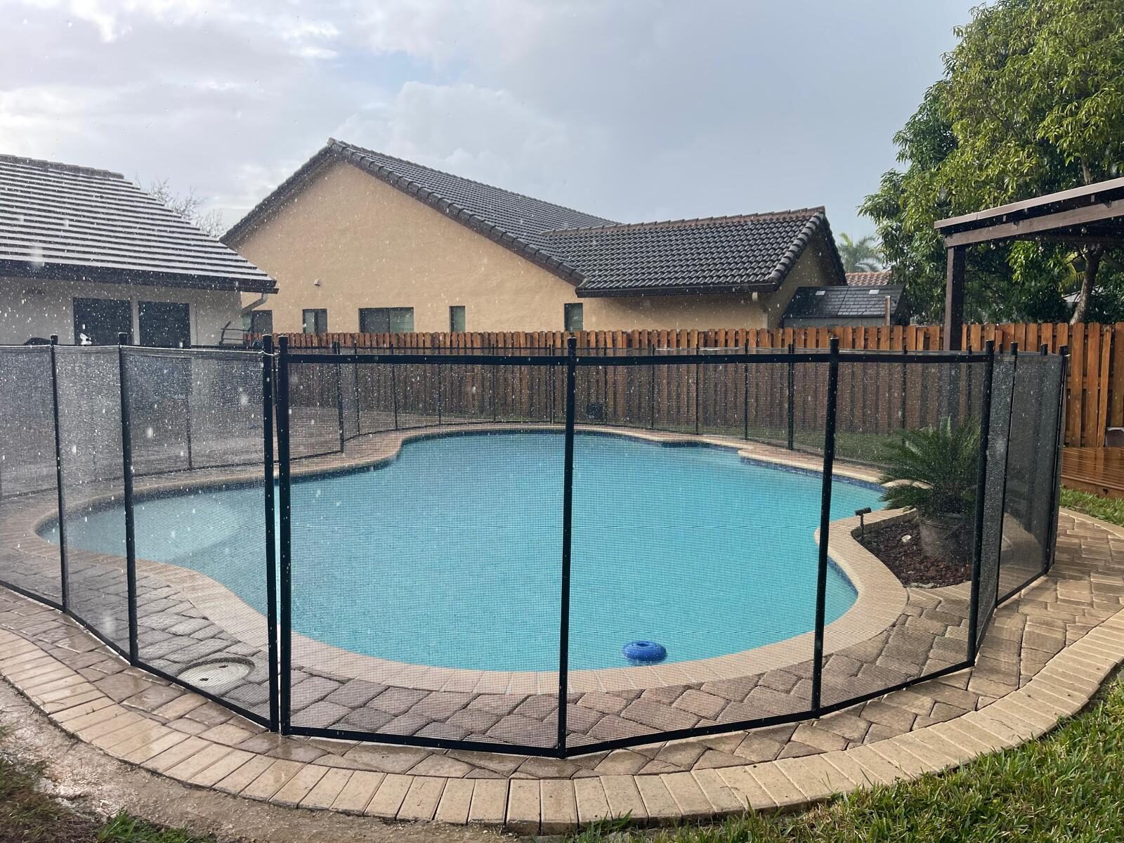 Black mesh pool fence surrounding a curved pool on a paver deck in Pembroke Pines