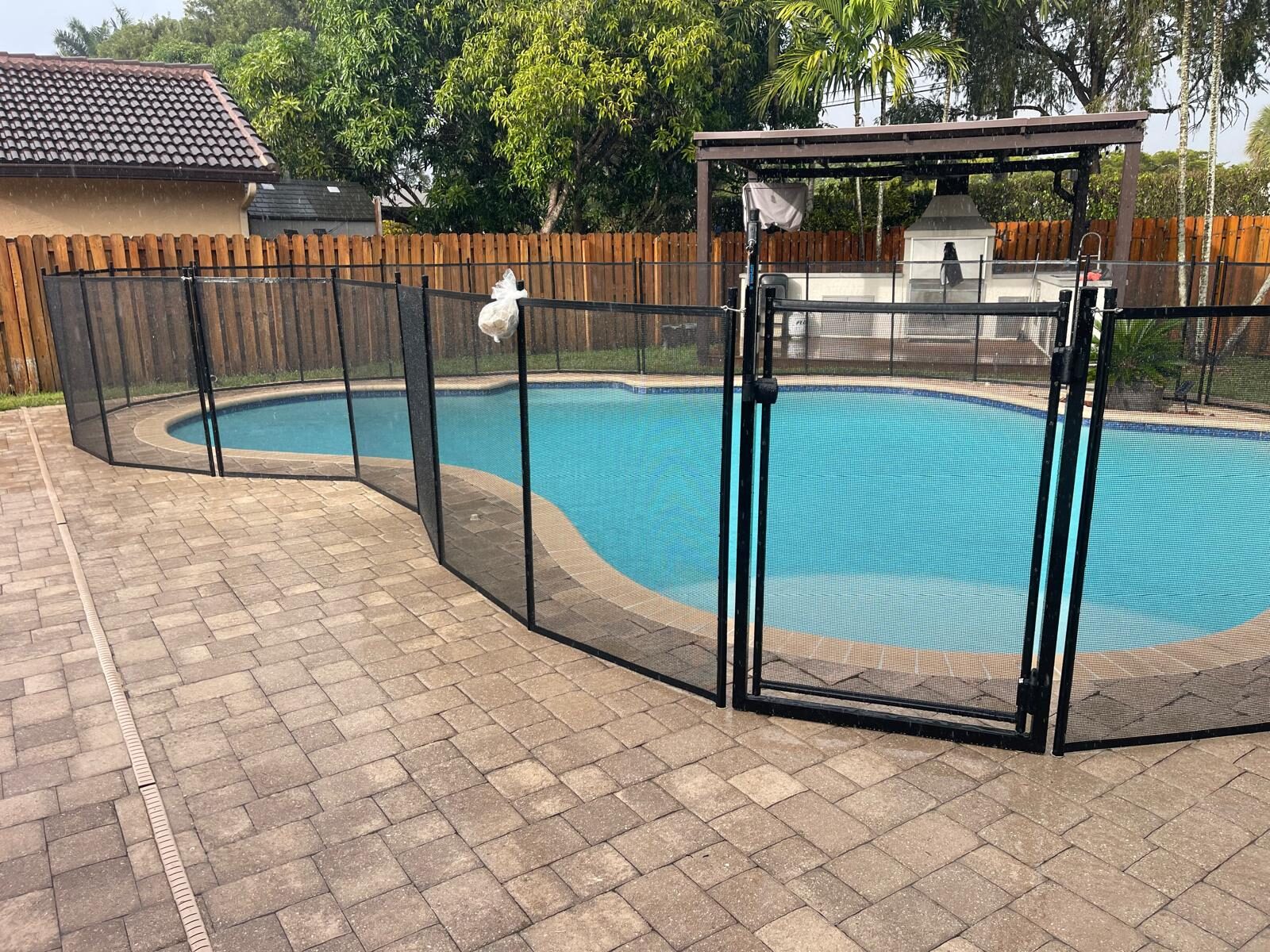 Barrier planning for visiting grandchildren: black mesh fence and gate beside a curved Pembroke Pines pool