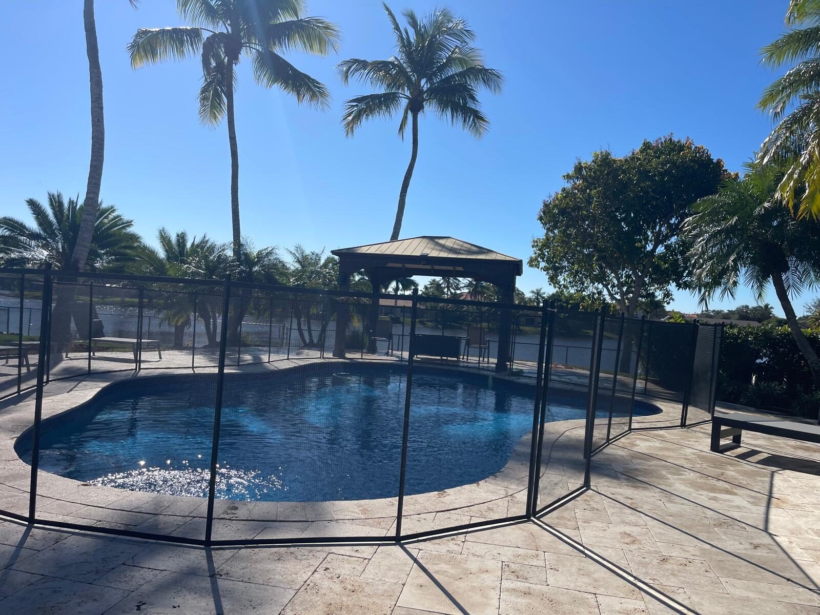 Black mesh pool fence around a curved pool with a gazebo and lakeside patio in Pembroke Pines