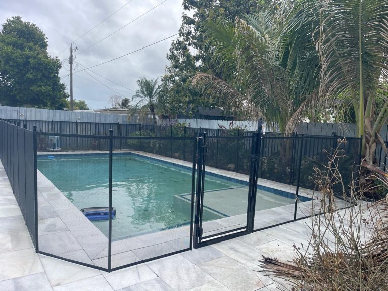 Black mesh pool fence and gate beside a rectangular pool on a pale tiled deck in Pembroke Pines