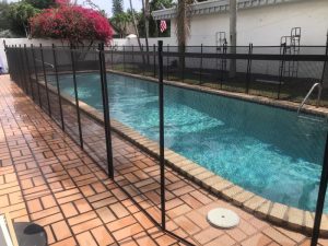Pool fence Plantation guide example: black mesh fence beside a rectangular pool and brick deck