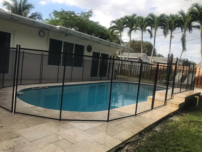 Black mesh fence around a curved pool beside a pale stone deck and steps
