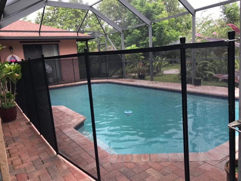 Black mesh pool fence inside a screen enclosure around a blue pool and brick deck