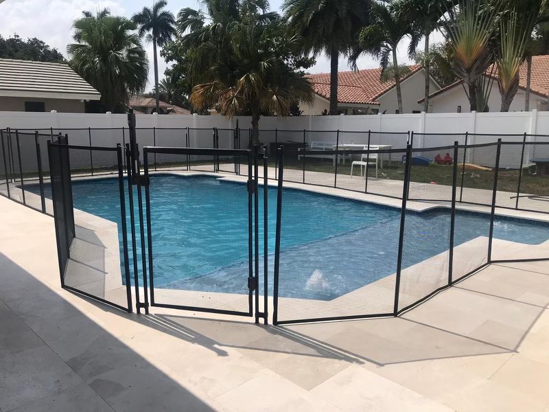 Black mesh pool fence gate with adjacent posts and panels on a light deck