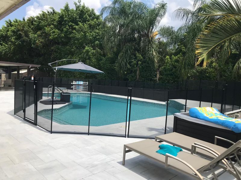 Black mesh pool fence and gate beside a pale patio deck