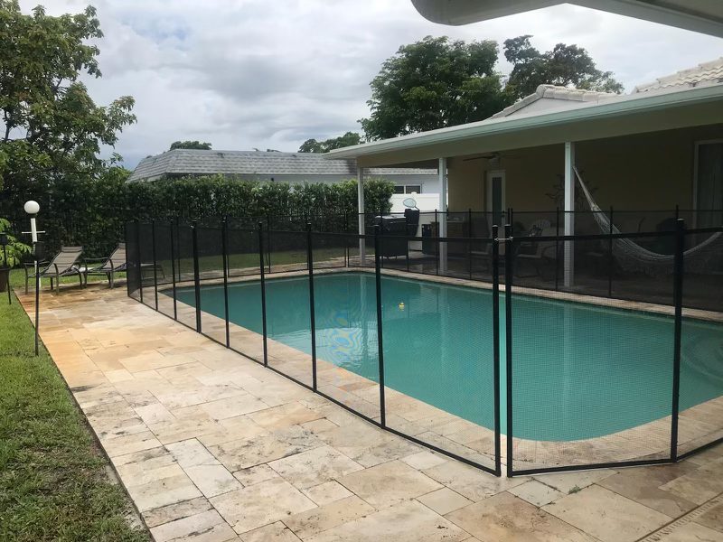 Mesh pool fence around a rectangular pool beside a covered house patio