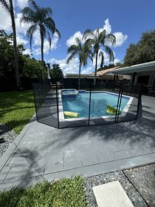 Black mesh pool fence and gate around a blue pool and raised spa in Plantation