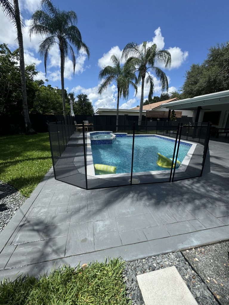 Black mesh pool fence and gate around a blue pool and raised spa in Plantation