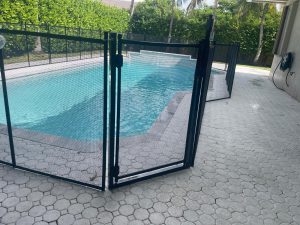 Black mesh pool gate with visible hinges and latch post on a Weston paved deck